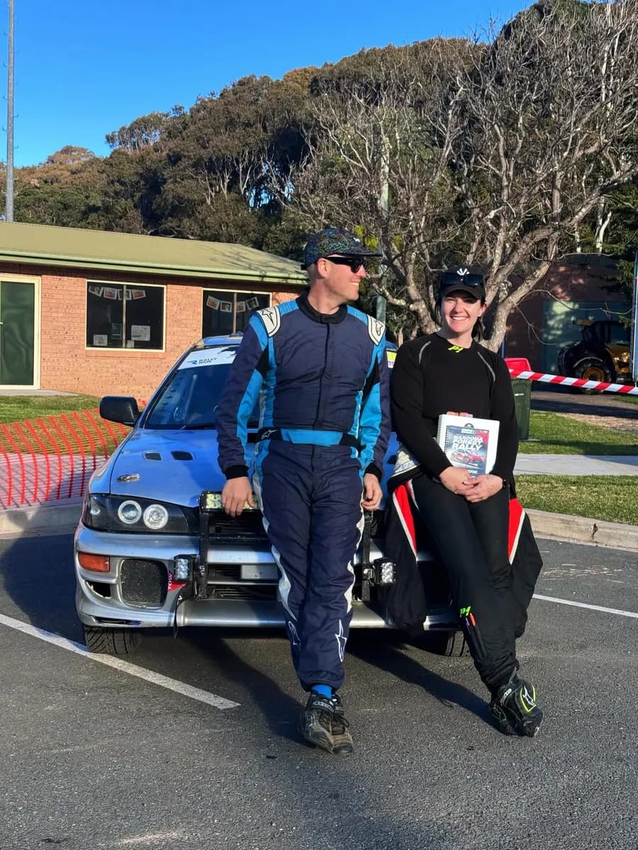 Rally driver Michael Chora and co-driver Rachael Ferrante in race suits beside their Subaru rally car, 2026