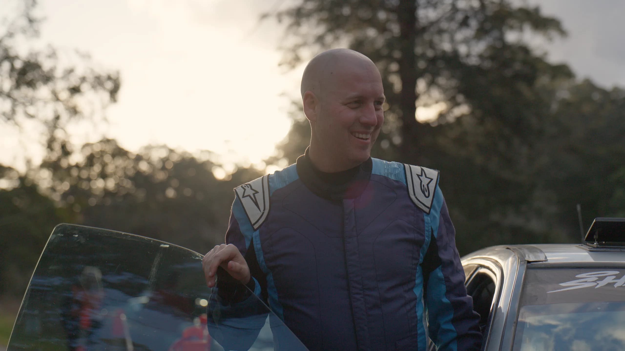 Michael Chora in race suit beside the car at the Ada River Rally
