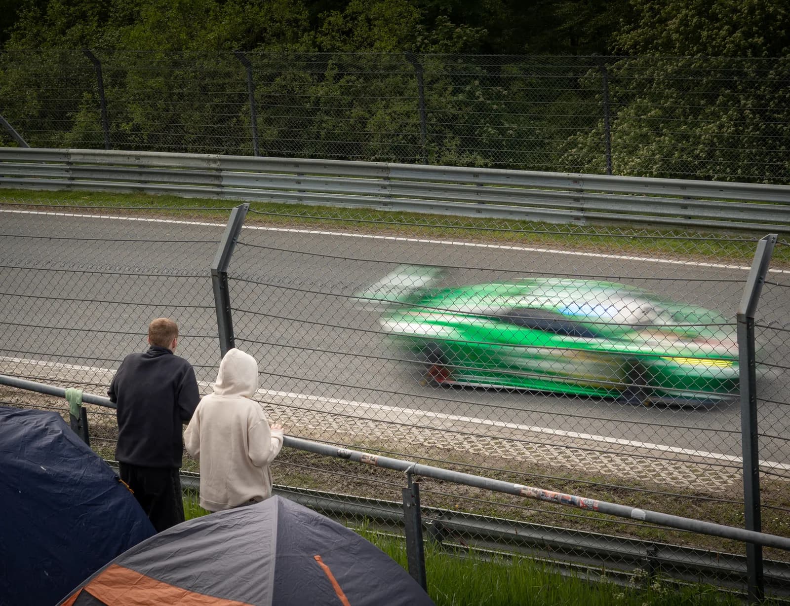 A green GT3 car panned at speed past spectators at the Nürburgring 24 Hours