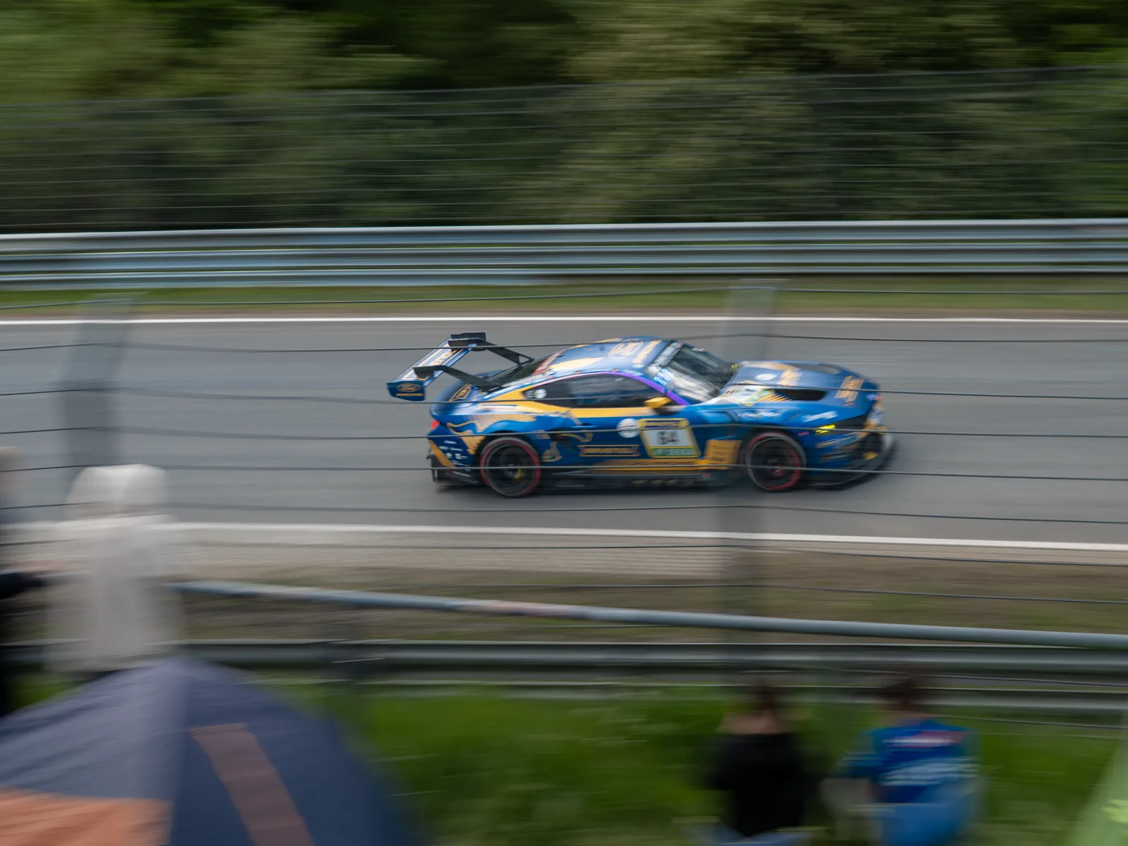 A blue GT3 race car at speed past the fence at the Nürburgring 24 Hours