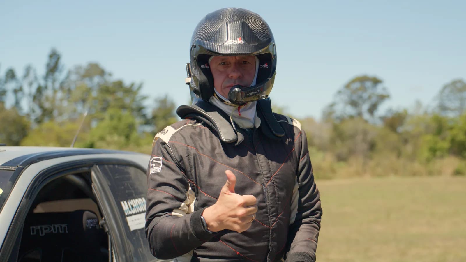 A Shakewell Racing crew member in helmet and race suit gives a thumbs up at the Imbil Rally